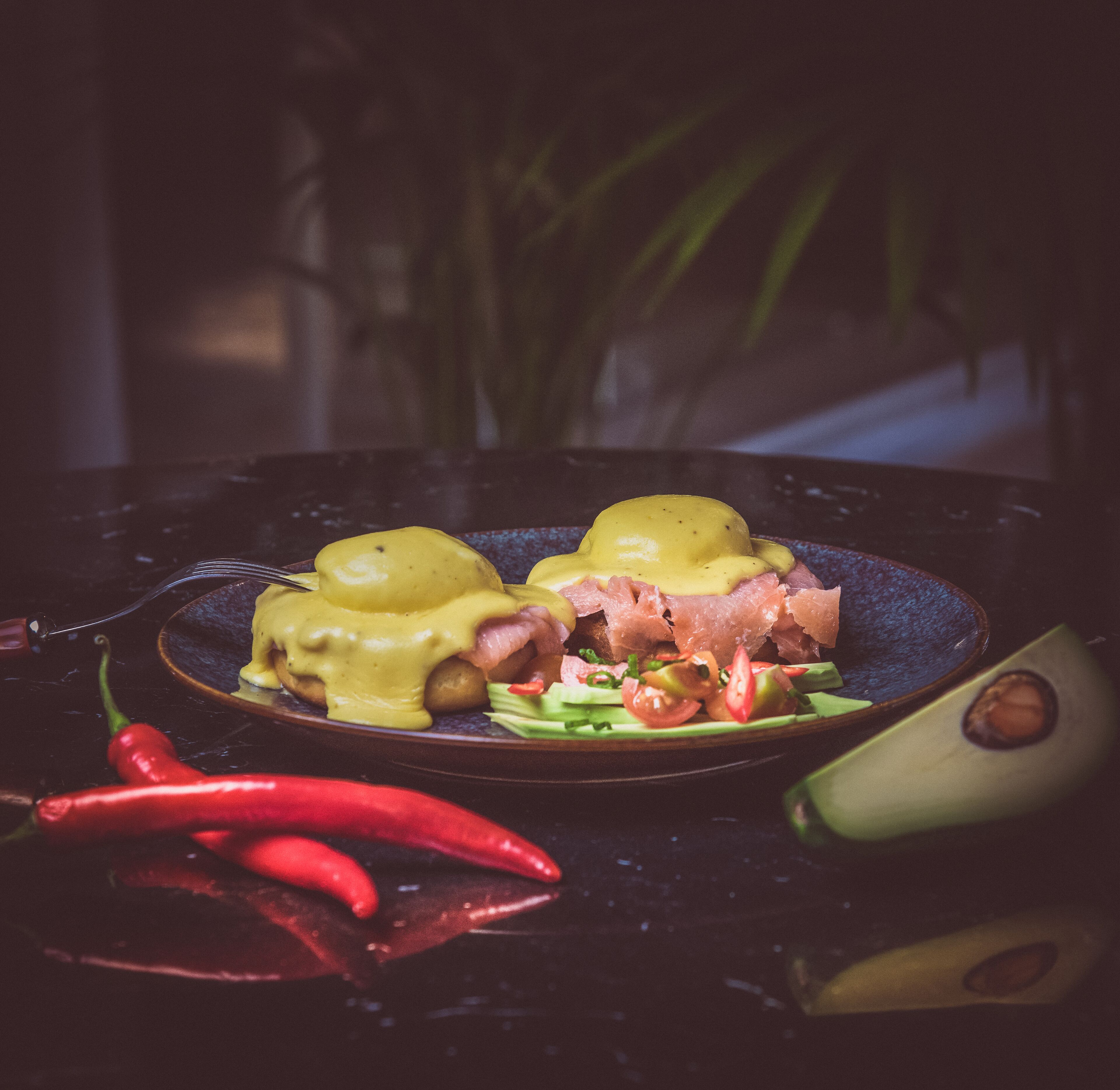 A plate of eggs benedict with ham and a side of avocado and tomatoes.