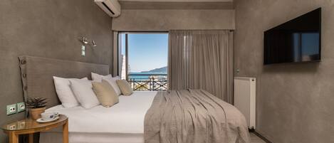 Habitación de hotel moderna con una cama grande, un televisor, una mesita con una taza y un platillo, y vista al mar a través de una ventana.