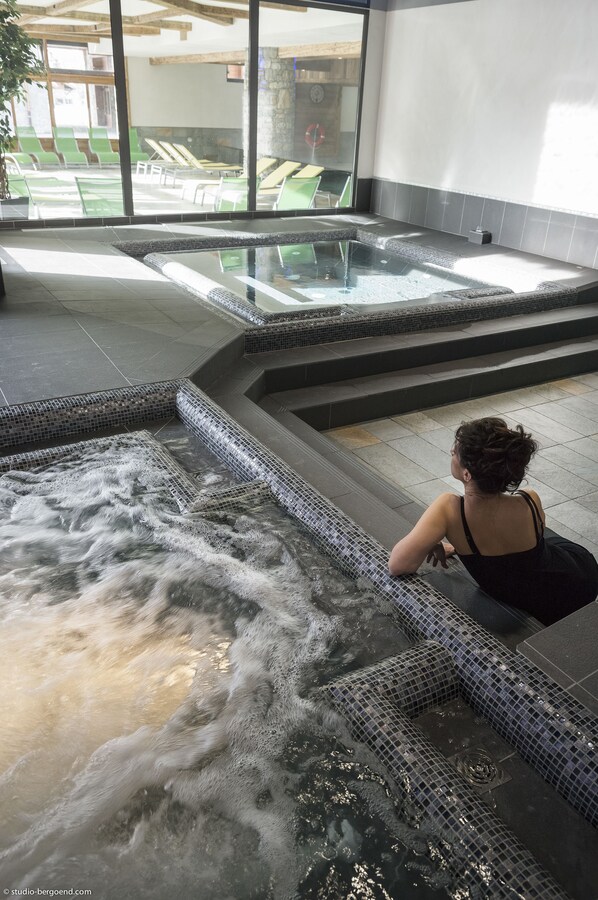 Un área de spa con hidromasaje y piscina, rodeada por paredes de vidrio y un muro de piedra.