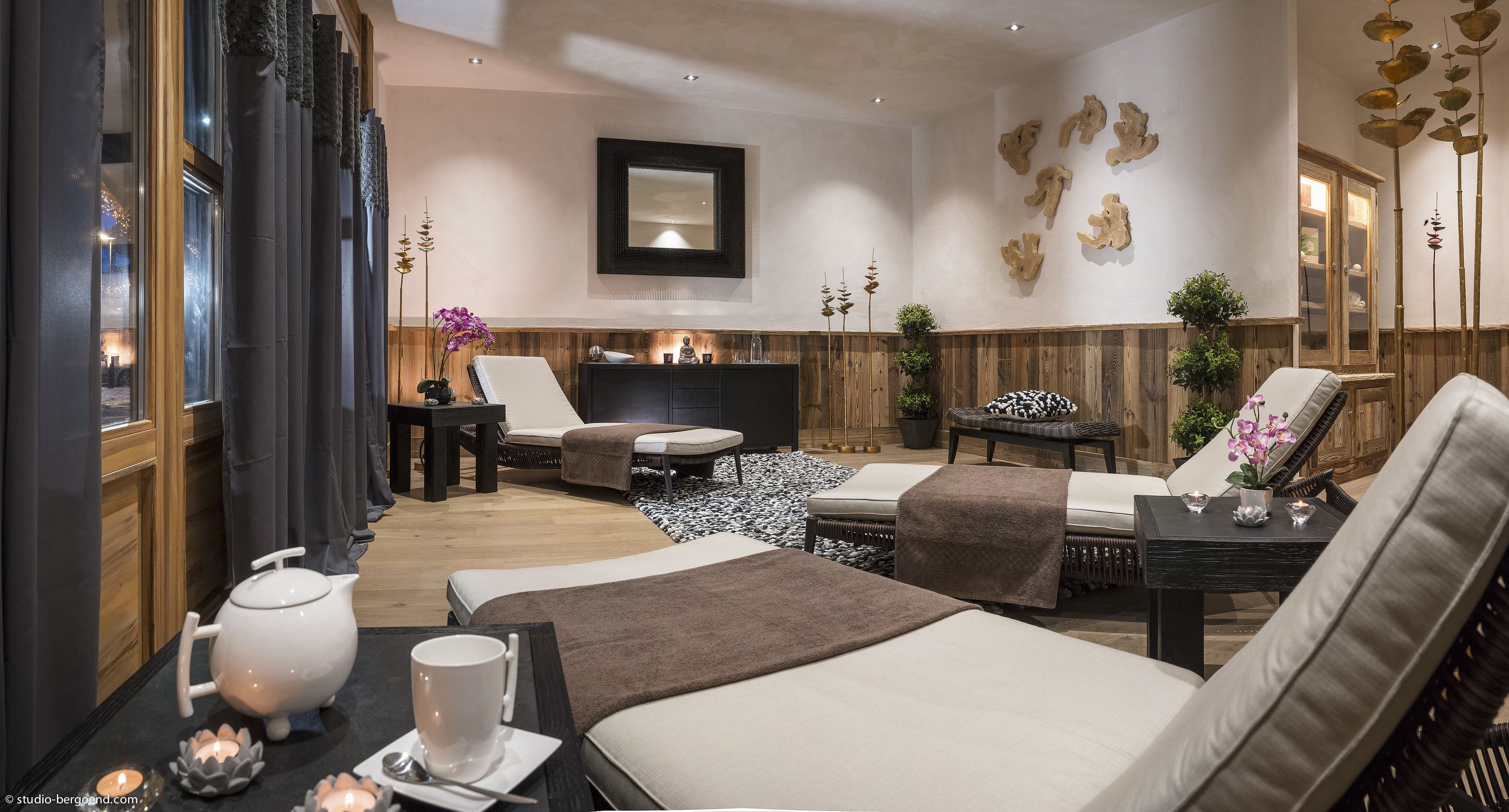A modern spa room with a large bed, a massage table, a small sofa, and a wooden cabinet.
