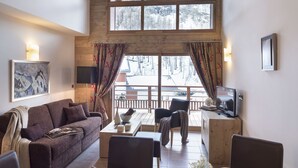 Un salon chaleureux avec un plafond en bois, de grandes fenêtres, un canapé, une table basse et un téléviseur.