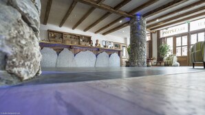 Un hall d’entrée spacieux avec un pilier en pierre, des poutres en bois au plafond et un comptoir d’accueil.