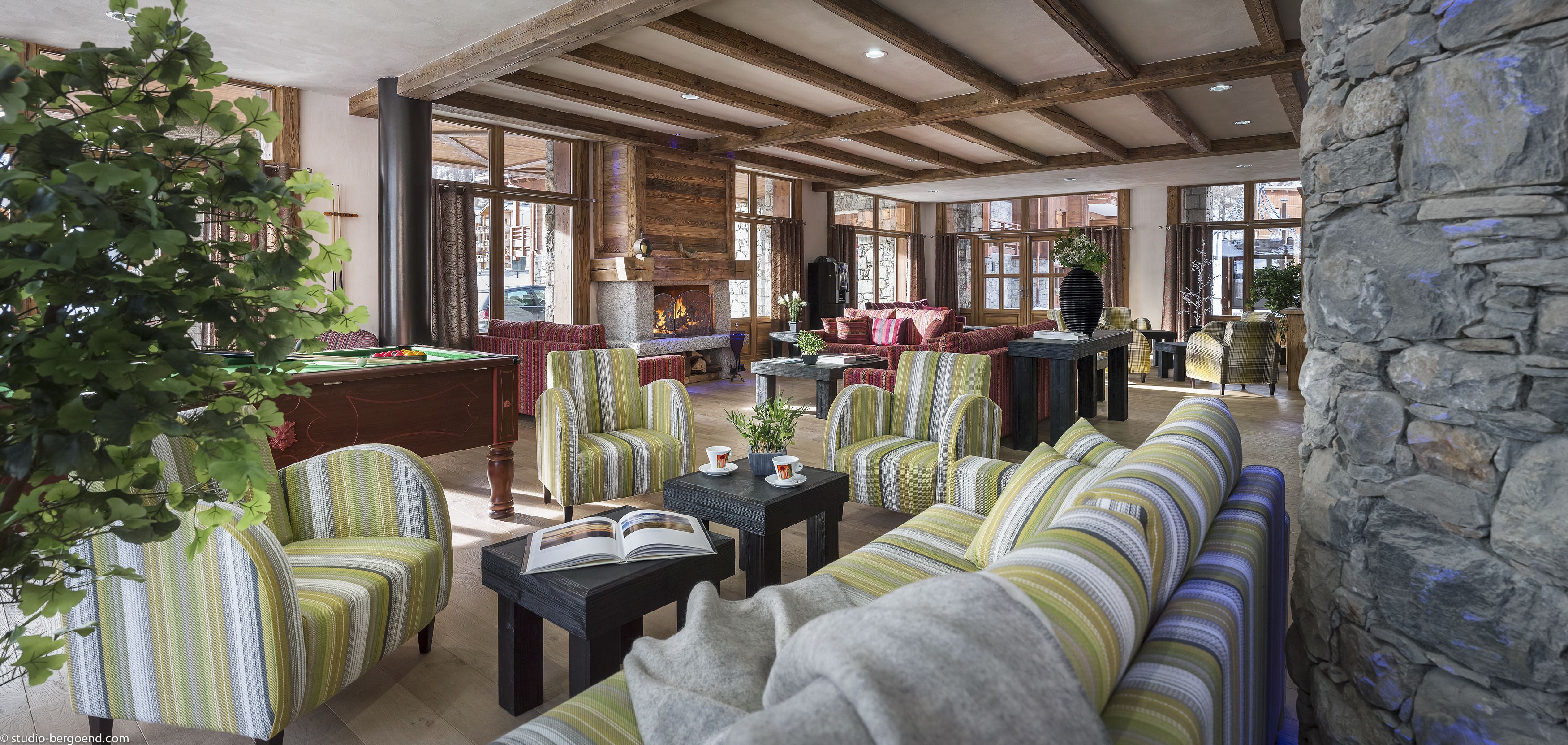 A spacious lounge with striped upholstered sofas, a fireplace, and large windows offering views of the outside.