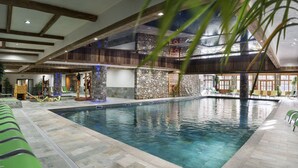 Une piscine intérieure aux murs en pierre, avec des poutres en bois et des fauteuils de détente verts.