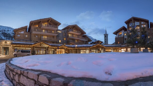 Un grand bâtiment en bois à plusieurs étages, doté de balcons, d’une entrée en pierre et d’un sol recouvert de neige.