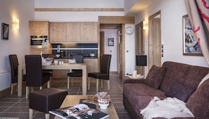Ein modernes Wohnzimmer mit einem braunen Sofa, einem Essbereich mit Holztisch und -stühlen sowie einer Küche mit Holzausstattung und einer schwarzen Arbeitsplatte.