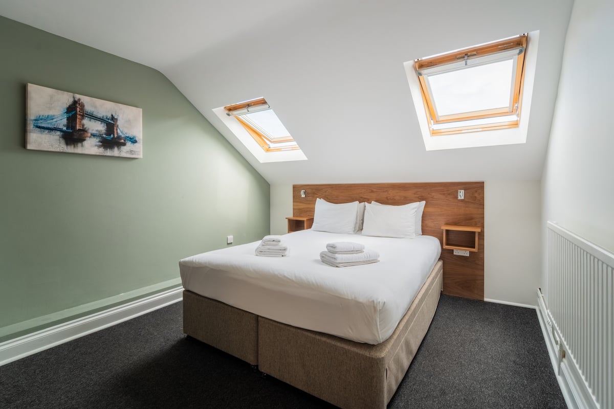 A bedroom with a large bed, two bedside tables, a wooden headboard, and two skylights.