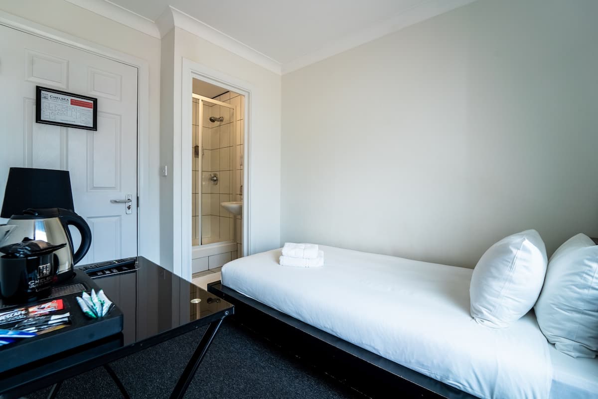 A hotel room with a bed, a desk with a coffee maker, a shower, and a framed certificate on the wall.