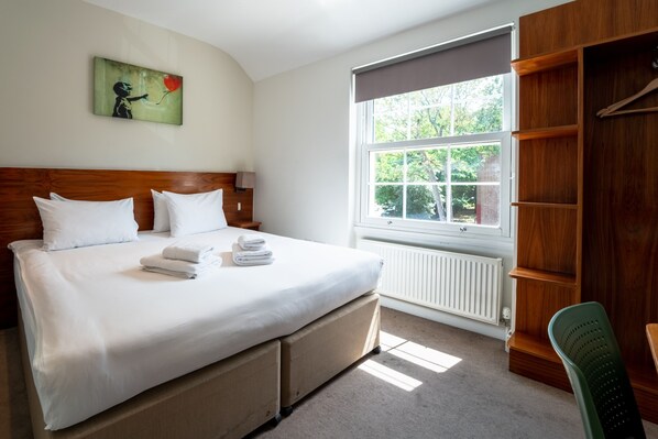 Ein Hotelzimmer mit einem großen Bett, einem Holzkopfende, einem Fenster mit Blick ins Grüne und einem Kleiderschrank.