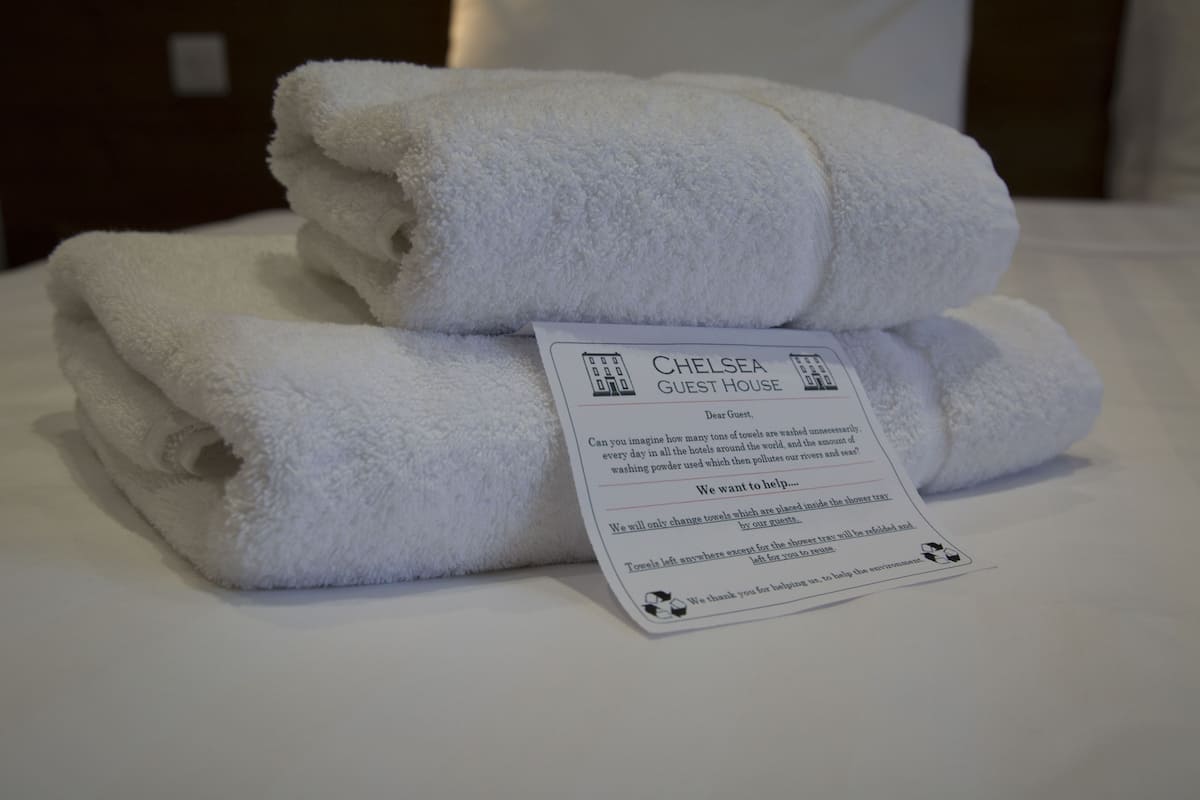 A stack of white towels on a bed with a sign about towel usage at Chelsea Guest House.