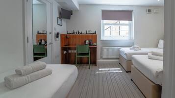 A hotel room with two single beds, a desk with a chair, a radiator, a window with a view, and a television on the wall.