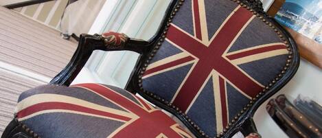 A chair with a Union Jack design, positioned in a room with a striped carpet and a glass door leading to a staircase.