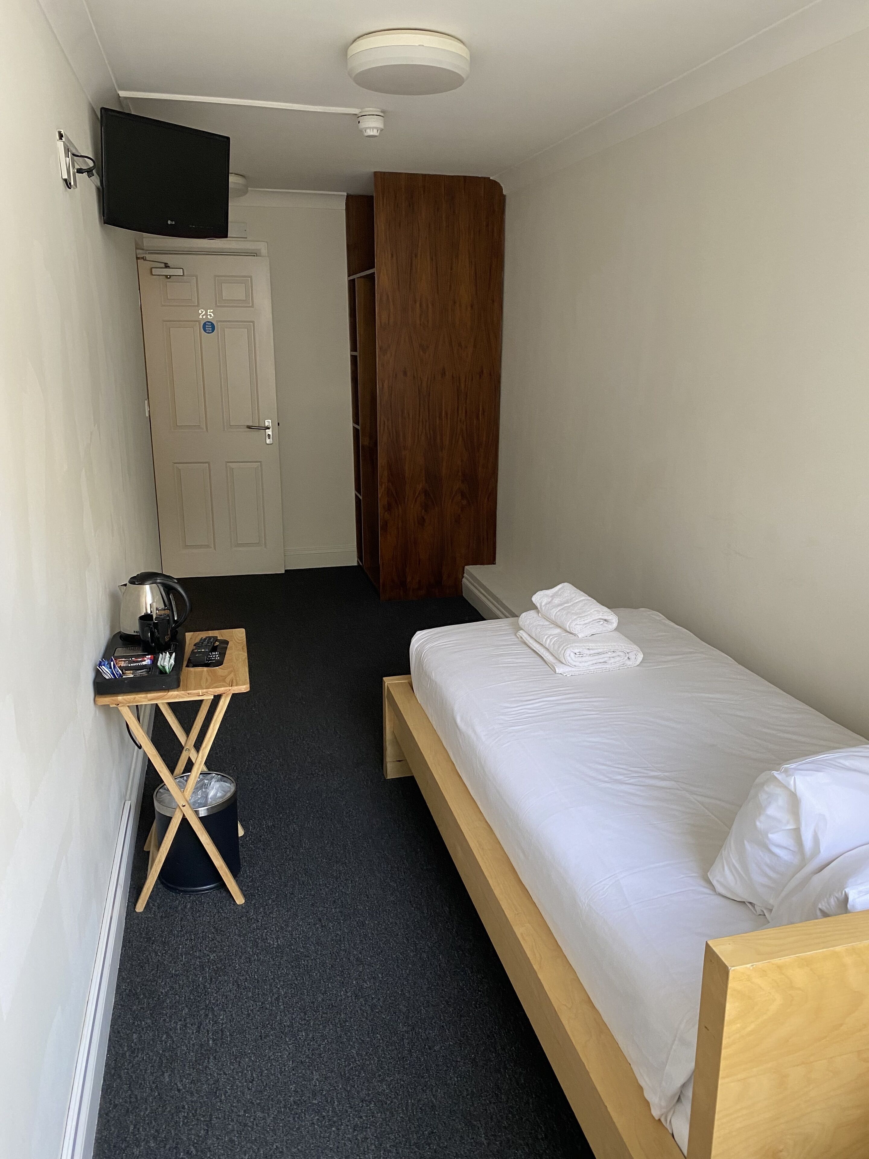 Een kleine, schone kamer met een bed, een bureau, een televisie en een kledingkast.