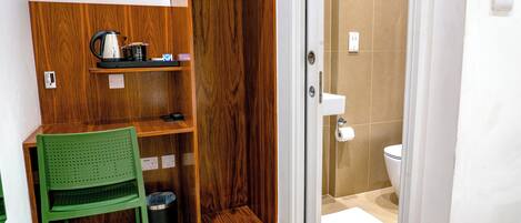 Un baño pequeño y funcional con ducha, inodoro y una zona de descanso con una silla y un cubo de basura.