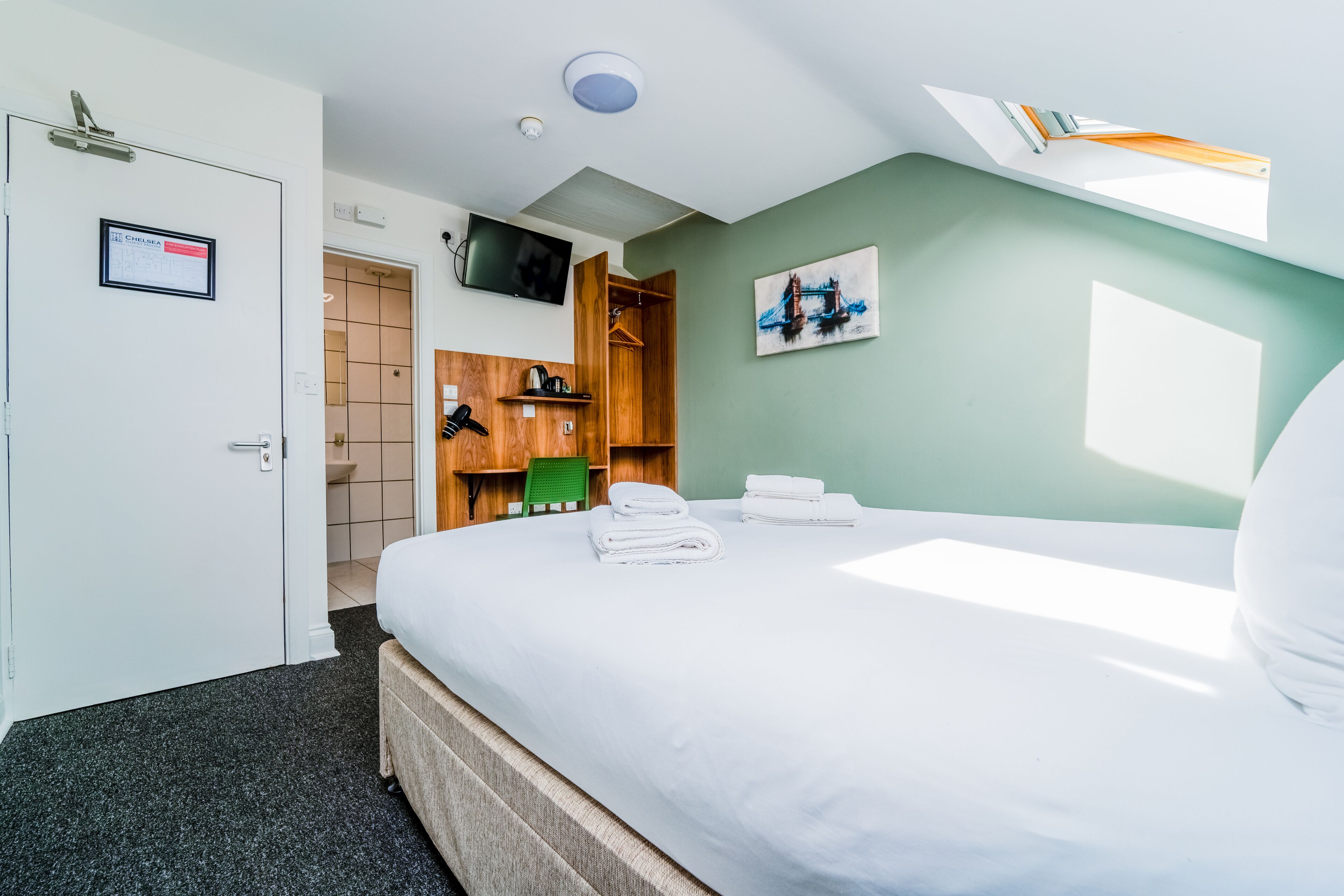 A hotel room with a bed, a television, a painting, and a wooden wardrobe.