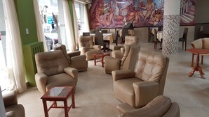 A spacious lobby with leather armchairs, a glass coffee table, and a large mural on the wall. - Hotel Catedral (Mar del Plata)