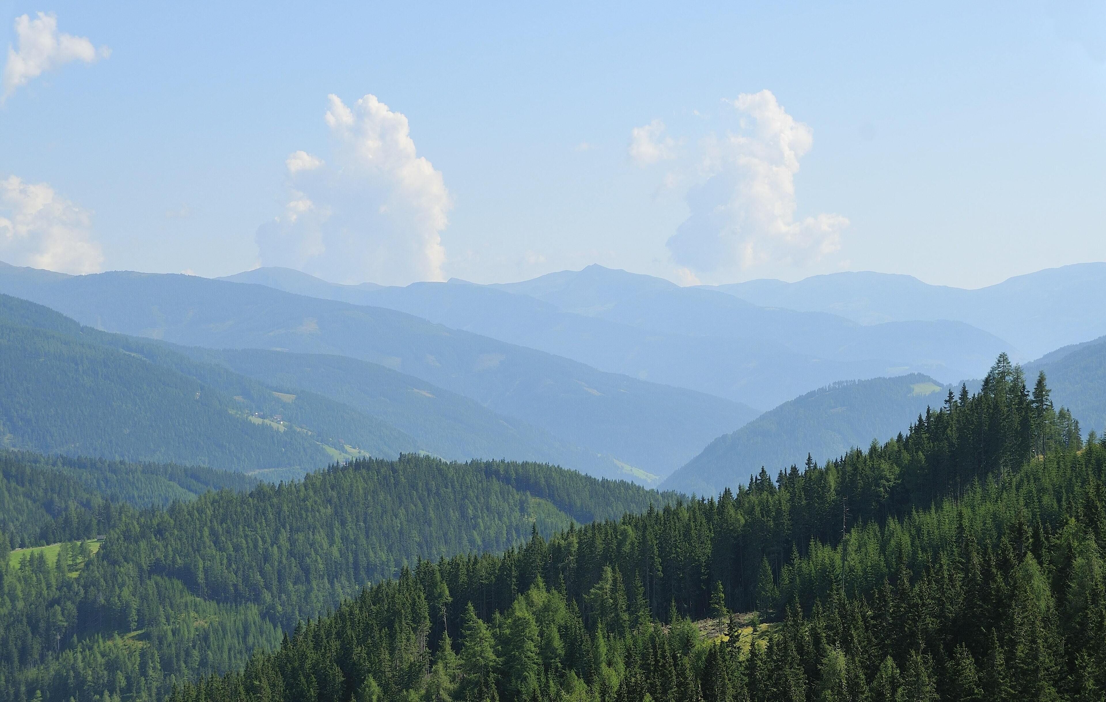 A mountainous landscape with dense forests and distant hills.