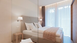 Habitación de hotel moderna con una cama grande, lámparas de noche, una mesita con una toalla y un ventanal con cortinas.