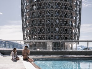 A pool area with a view of a mountainous landscape and a building with a unique lattice structure. -  Falkensteiner Residences Edelweiss (Rennweg am Katschberg)