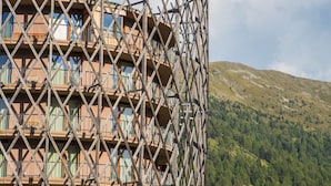 Un edificio de varios pisos con una fachada de celosía singular, balcones y un telón de fondo montañoso.