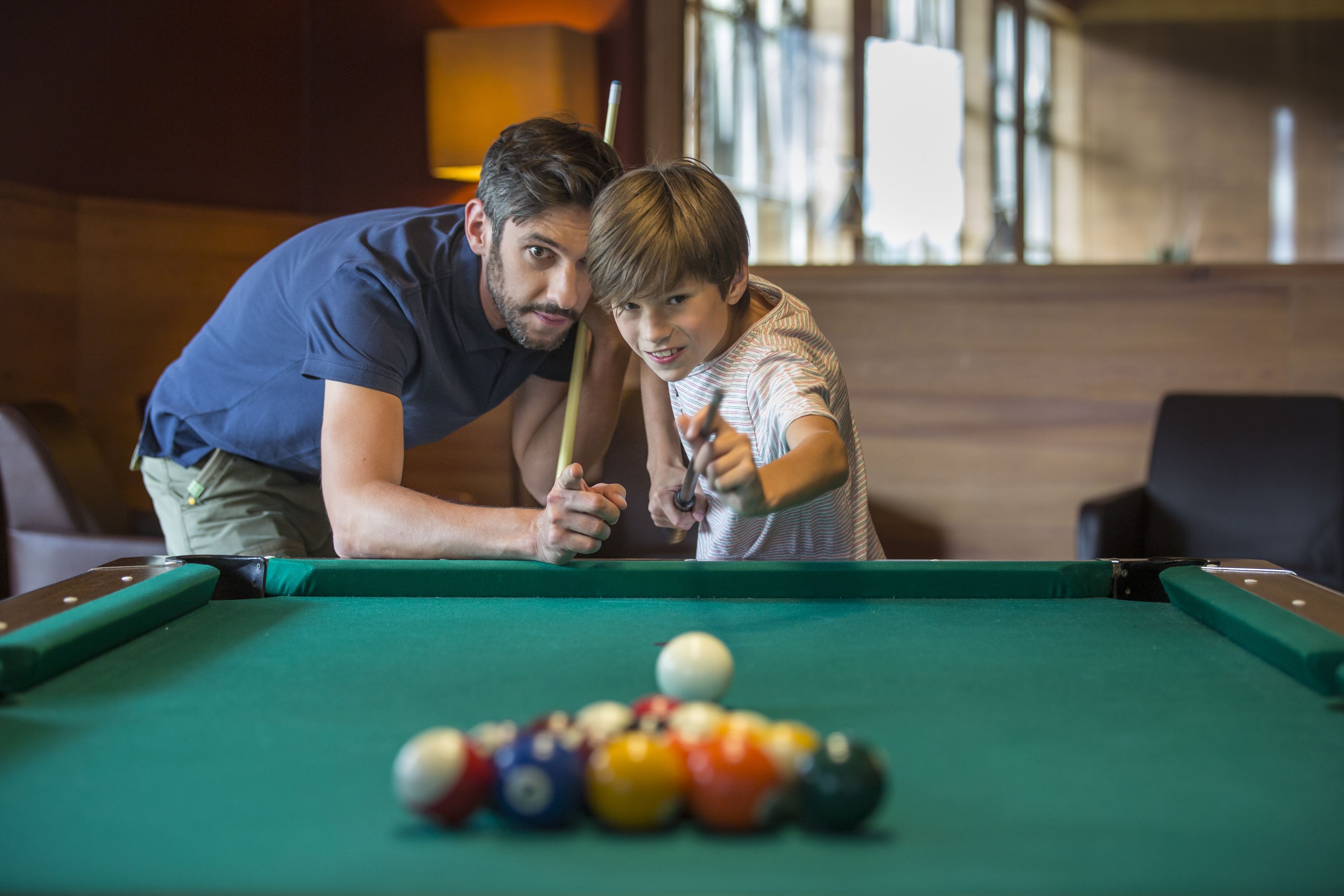 A pool table with a cue stick and balls, a person leaning over the table, and another person standing beside it.