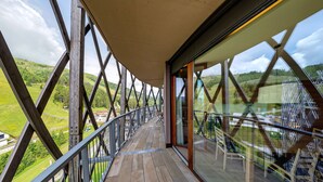 Una terraza de madera con barandas de vidrio que da a un paisaje verde.