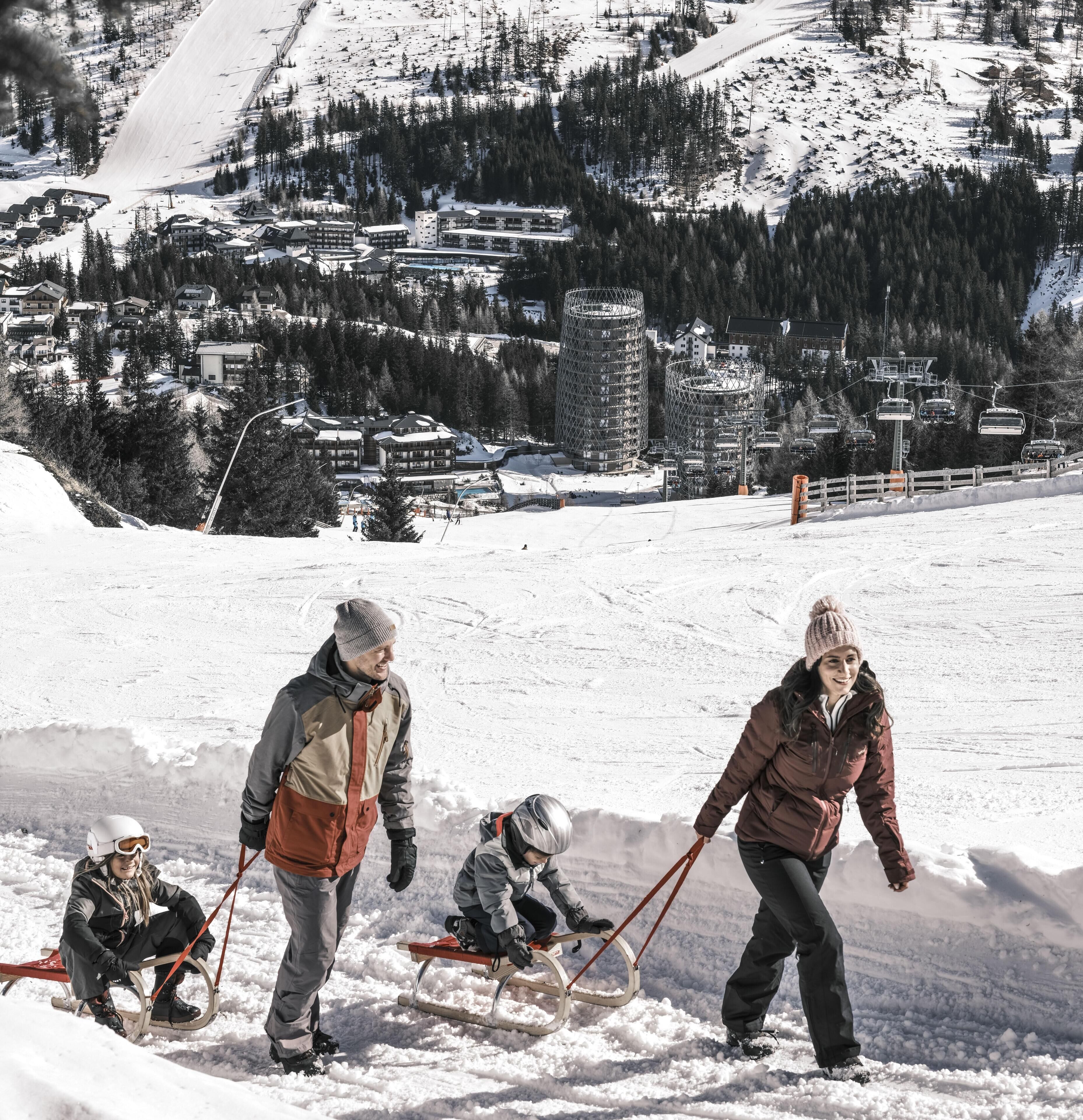A family sledding on a snowy slope with a ski resort in the background.