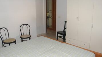 A bedroom with a bed, two chairs, a wardrobe, and a door leading to another room.