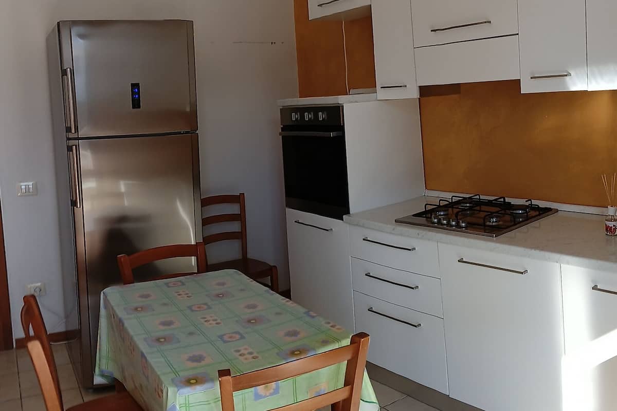 A compact kitchen with a refrigerator, oven, and gas stove. There is a dining table with chairs and a patterned tablecloth.