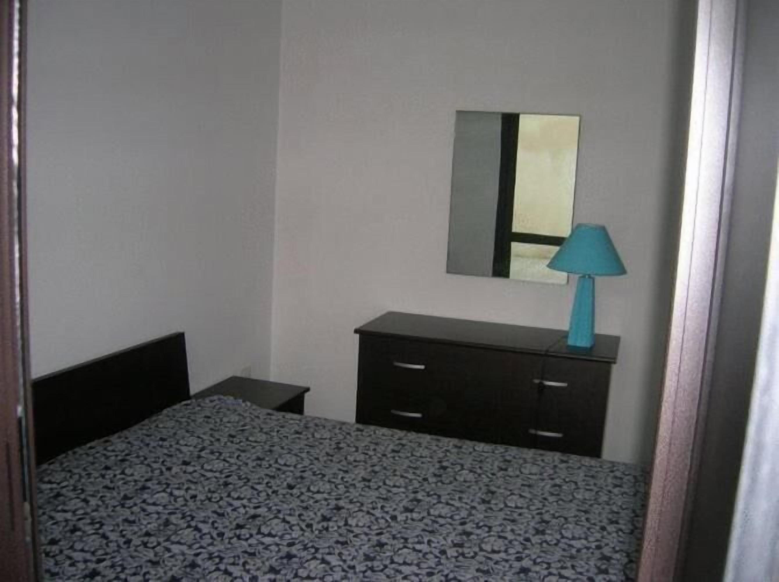 Une chambre à coucher avec un lit, une commode, un miroir et une lampe.