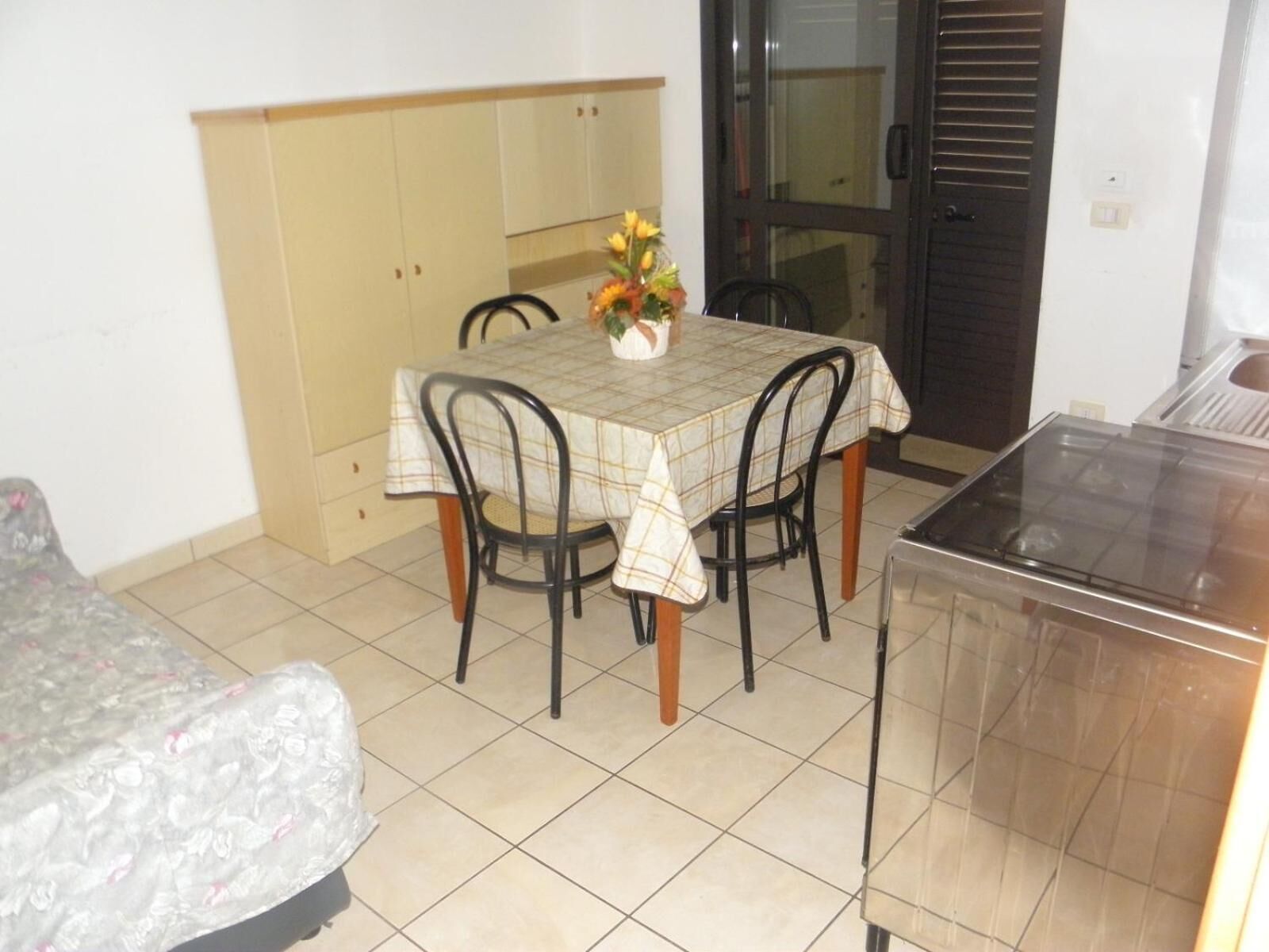 Een compacte kamer met een eettafel, stoelen, een kleine kitchenette en een bed.