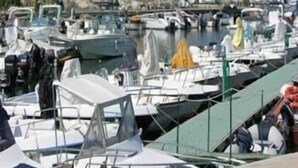 Uma marina com barcos atracados, uma torre de pedra imponente e edifícios ao fundo.