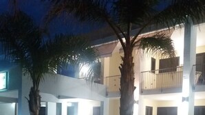 Um edifício de dois andares com varandas, palmeiras e uma entrada protegida por portão.