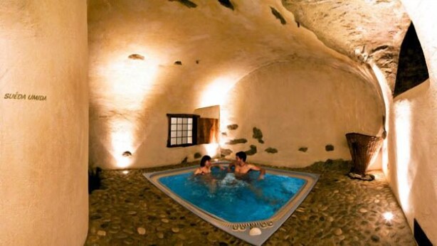 Una piscina interior con suelo de piedra y un ventanal pequeño.