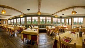 Un restaurante con interiores de madera, mesas redondas y amplios ventanales con vista a los árboles.