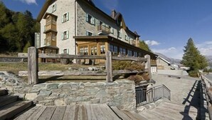 Un edificio de varios pisos con fachada de piedra, balcones de madera y una terraza delantera.