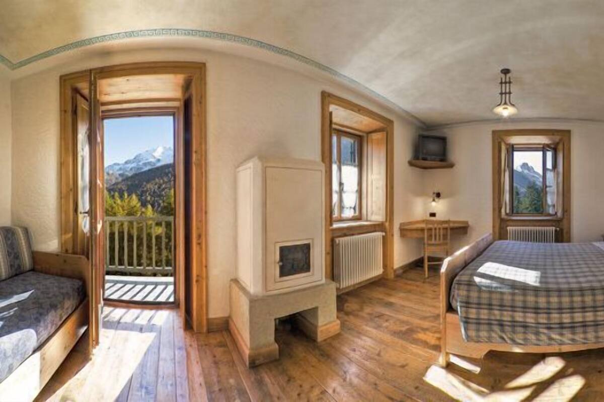 Ein Schlafzimmer mit einem Bett, einem Nachttisch aus Holz, einer Kommode, einer Heizung und einem Fenster mit Blick auf die Berge.