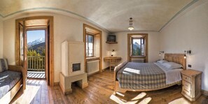 Un dormitorio con cama, mesita de noche de madera, cómoda, radiador y ventana con vista a la montaña.
