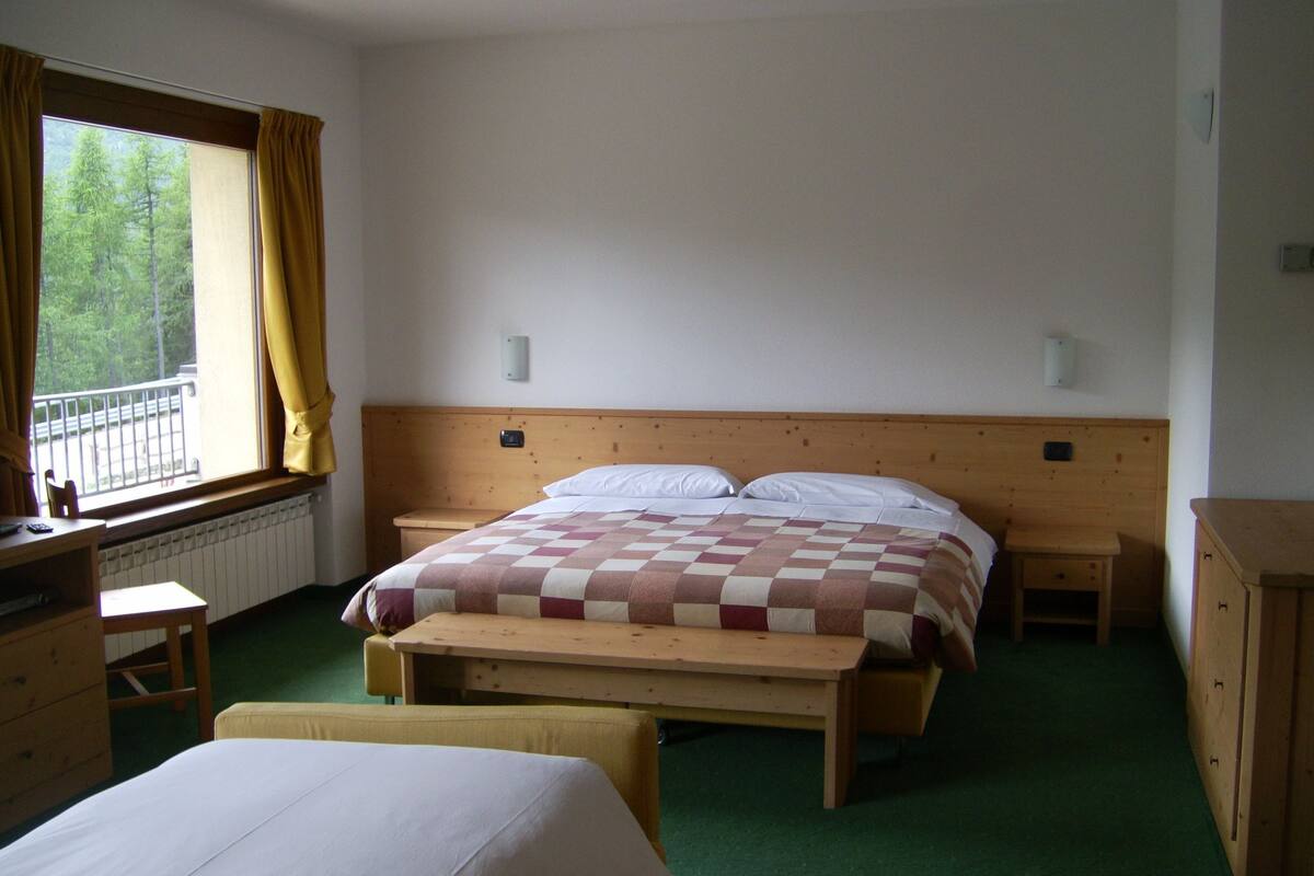 Ein Schlafzimmer mit einem hölzernen Bett, einem Nachttisch, einem Sessel, einer Kommode und einem Fenster mit Vorhängen.