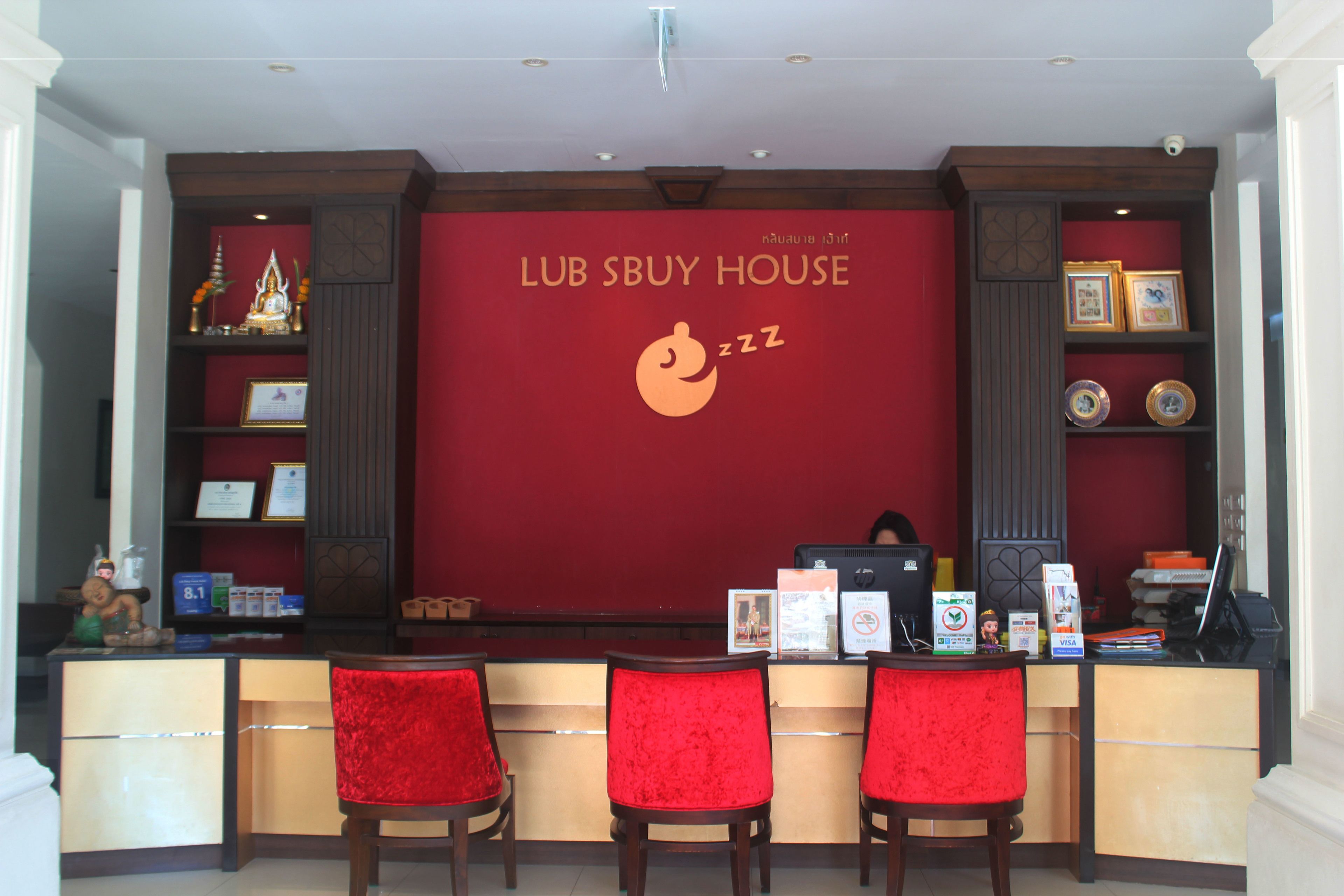 A reception area with a red wall, three red chairs, a counter with a computer, and various items on the counter.