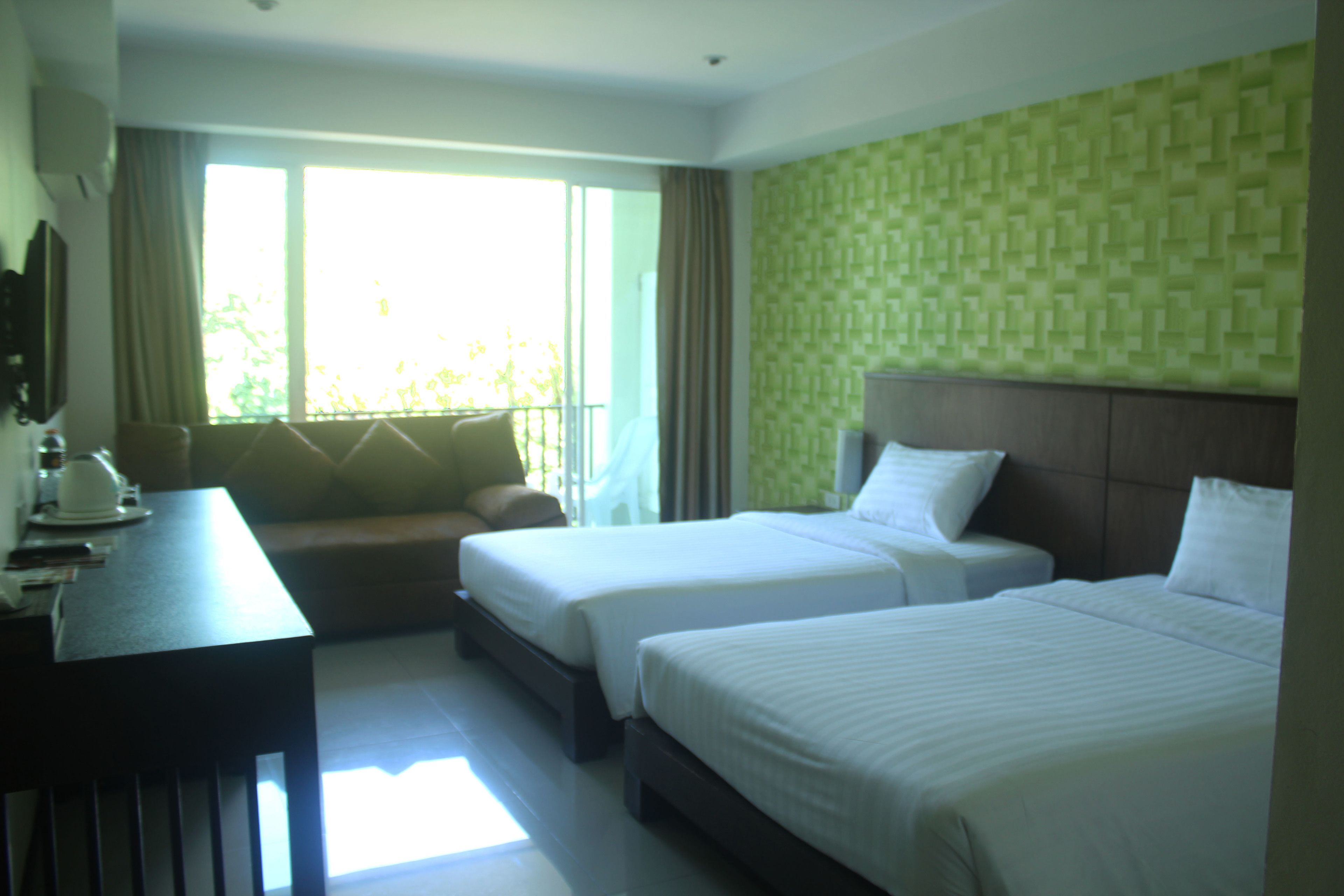 A hotel room with two beds, a desk, and a view of greenery outside.