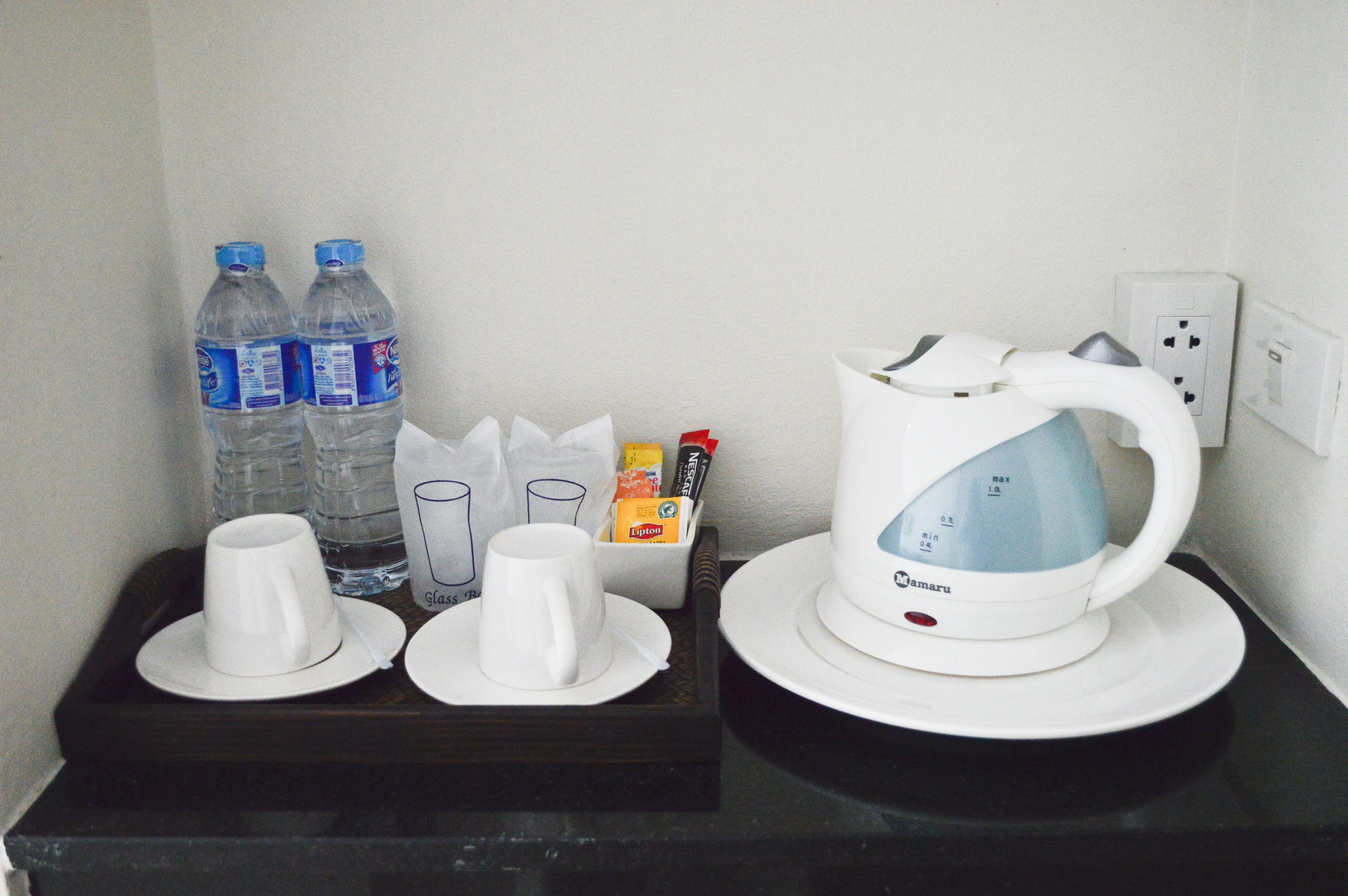 A tray with a white electric kettle, two water bottles, and two white cups on a black tray.