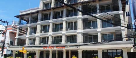 Un hotel de varios pisos con balcones, un restaurante en la planta baja y varios coches y motocicletas estacionados.