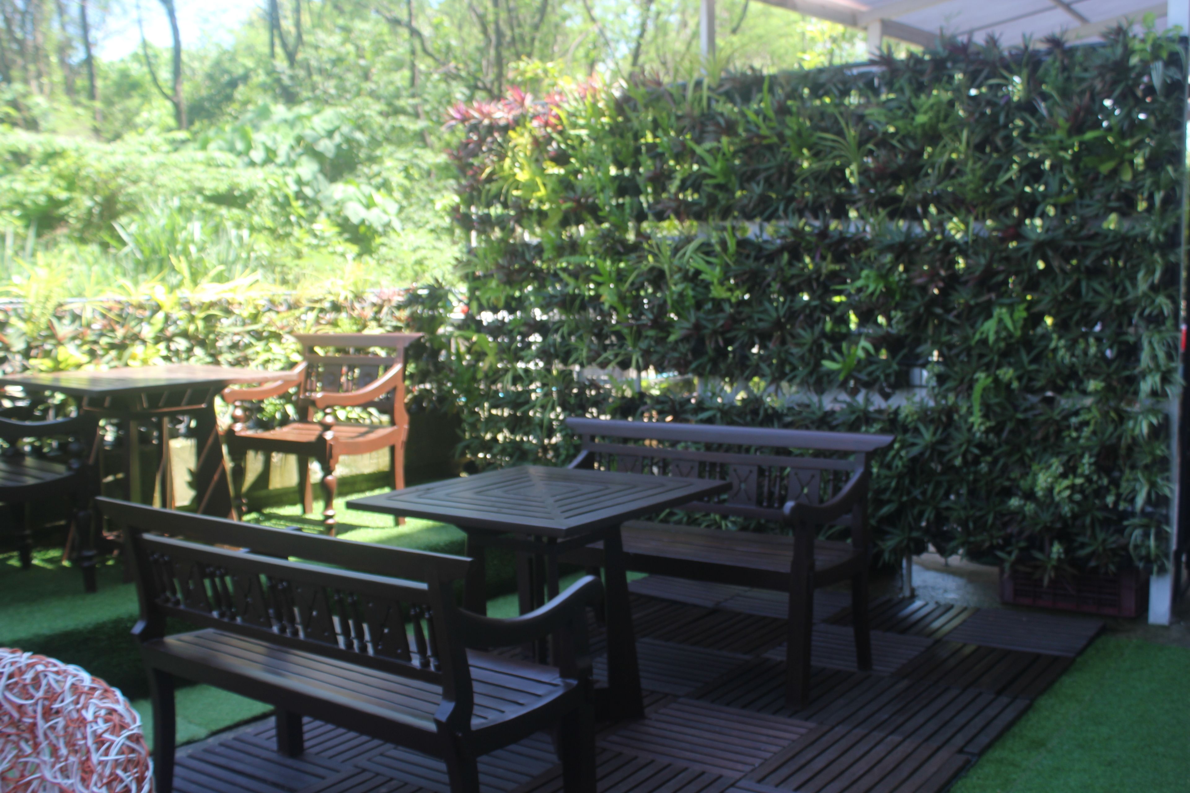 An outdoor patio area with wooden tables and benches, surrounded by lush greenery and a vertical garden wall.