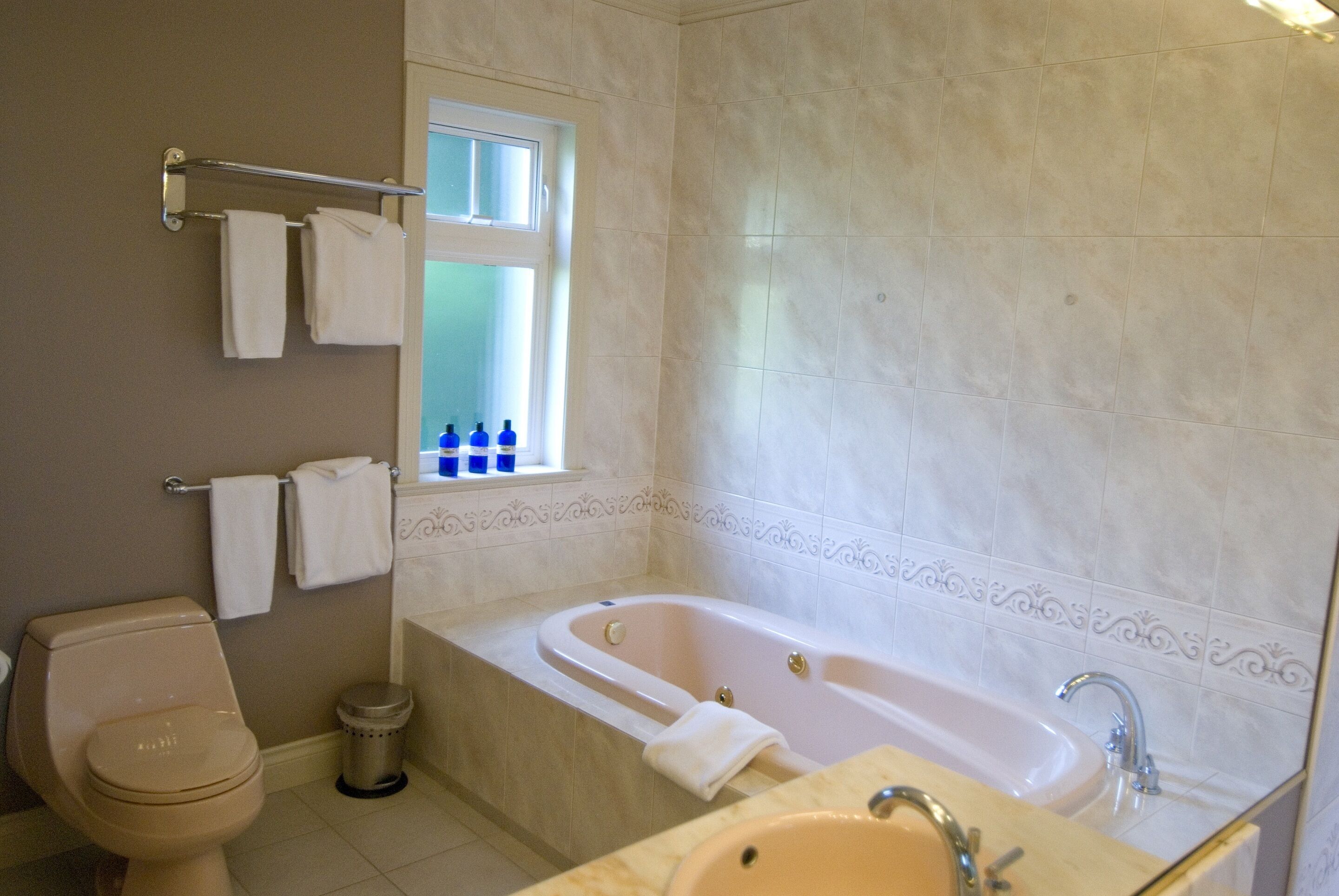 Un baño con inodoro, bañera, lavabo y una ventana con botellas en el alféizar.