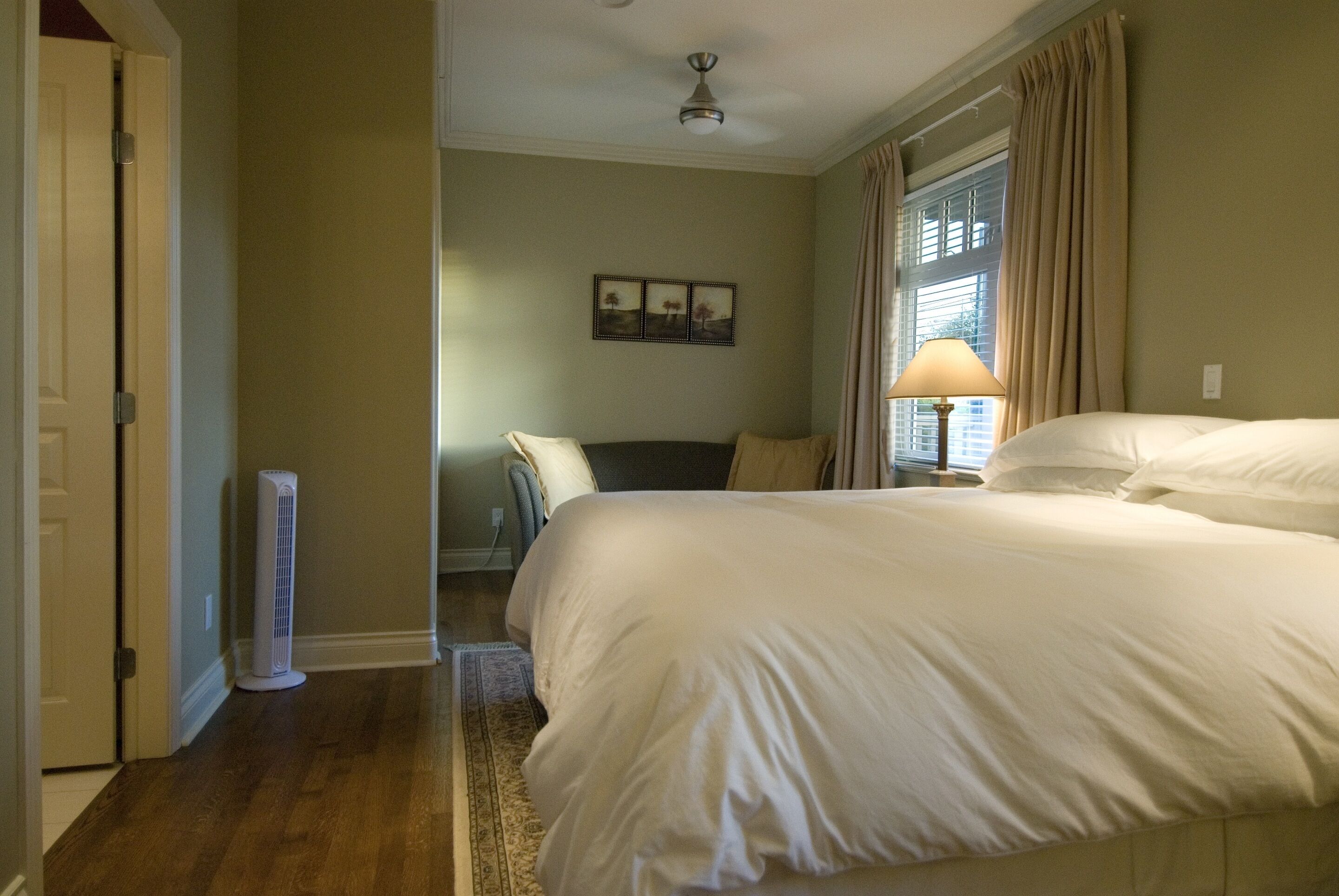 A bedroom with a large bed, a standing heater, a window with curtains, and a ceiling fan.