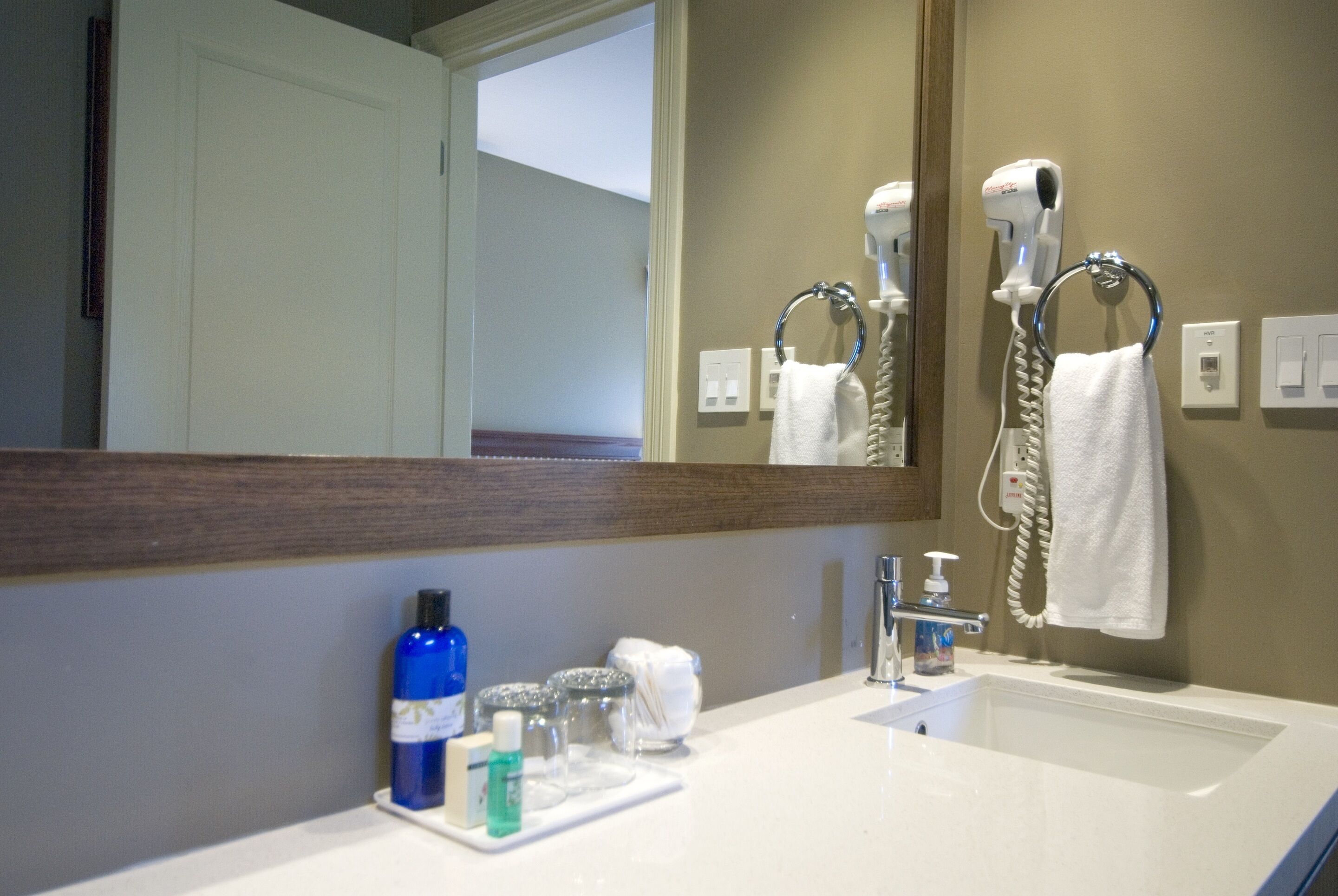 A bathroom with a white sink, a mirror, a hairdryer, and toiletries on the counter.
