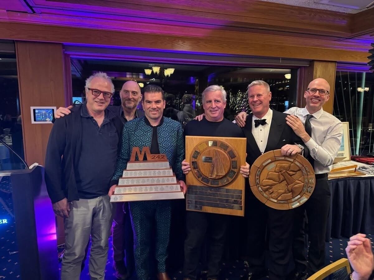 A group of people holding awards in a room with a wooden ceiling and a window.