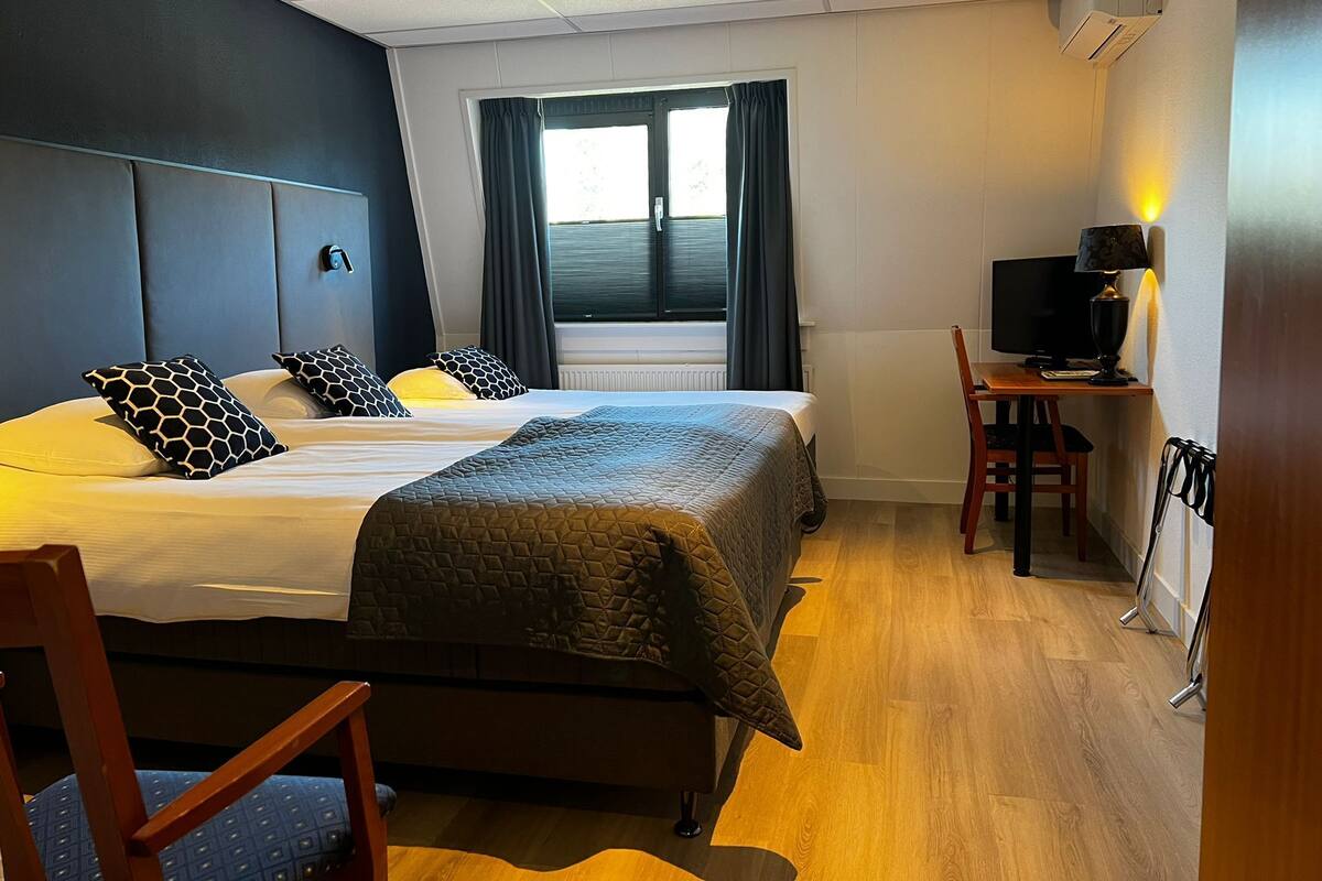 Una habitación de hotel con dos camas, un escritorio con ordenador, una silla y una ventana con cortinas.