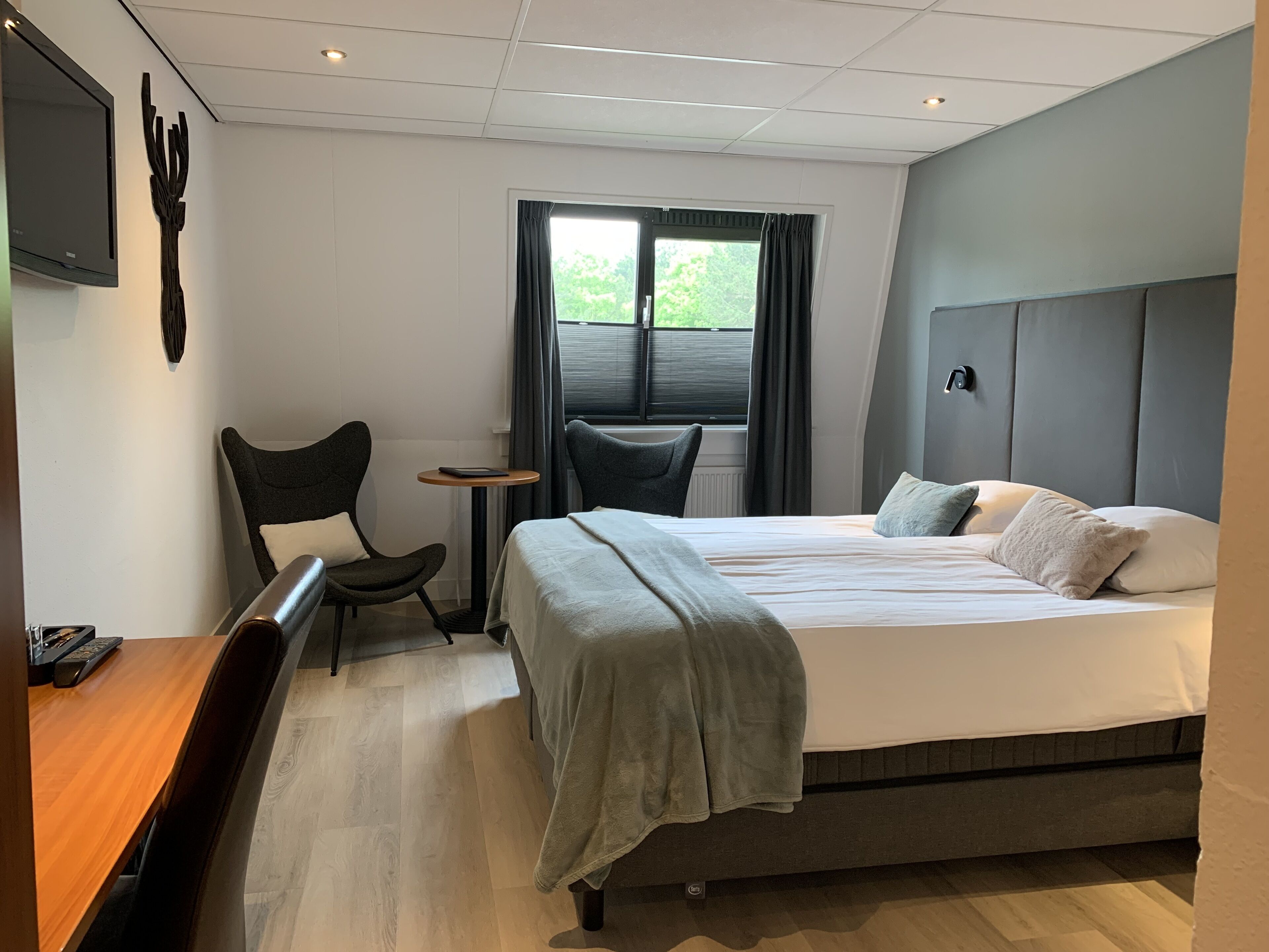 Quarto de hotel moderno com uma cama grande, uma escrivaninha, uma cadeira e uma mesinha.